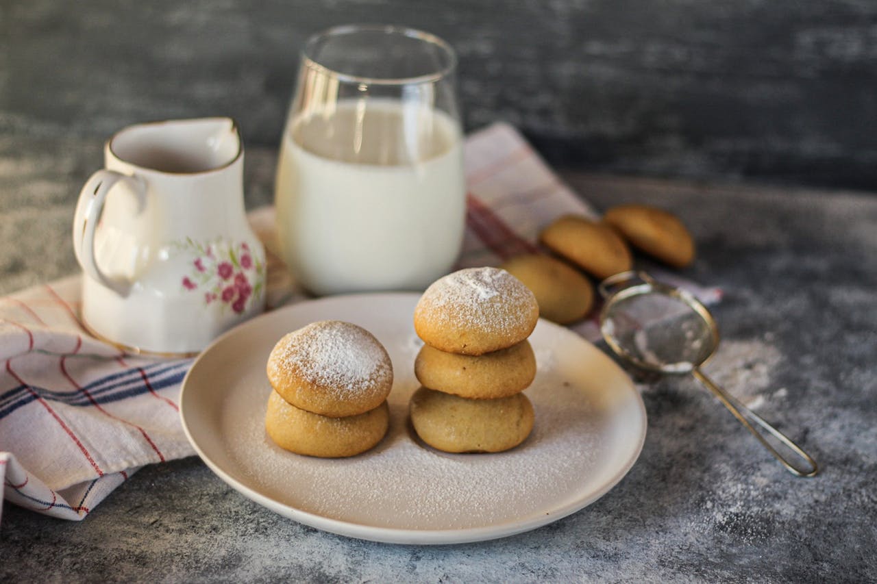 Delicious cookies sprinkled with powdered sugar, accompanied by a glass of milk and a decorative creamer.